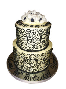 Two-tier red velvet cake with cream cheese buttercream, decorated with hand-piped black scroll designs and topped with white and black fondant fantasy flowers for an anniversary celebration