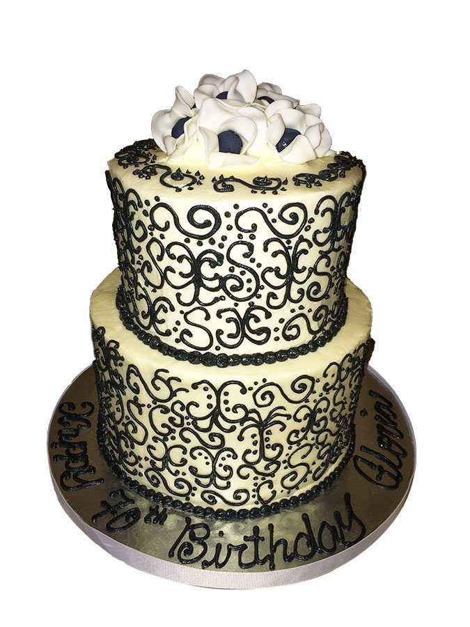 Two-tier red velvet cake with cream cheese buttercream, decorated with hand-piped black scroll designs and topped with white and black fondant fantasy flowers for an anniversary celebration