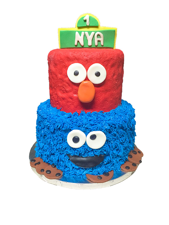 Two-tier Sesame Street birthday cake featuring a red fondant Elmo top tier and a blue buttercream Cookie Monster bottom tier decorated with fondant cookies, made for a first birthday celebration.